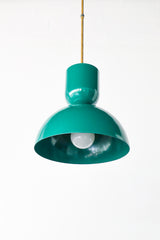 Deep emerald-green is the color that makes a kitchen feel rich and a little jewel-like, and this Taeuber pendant brings it in a punchy, sculptural shape. The two-part silhouette stacks a rounded cup over a wide domed bell, all finished in a glossy mermaid green with a warm brass stem, shown here lit and glowing against white brick. It reads saturated and confident, the kind of statement lighting that turns an island, breakfast nook, or sink into a focal point. 