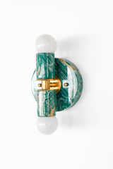 Thalia sconce in mermaid green, cream, and gold marbled finish, variation A, with round backplate and brass center detail, fitted with two globe bulbs. Compact statement wall sconce or flush mount ceiling light for bathroom vanity lighting, powder room decor, coastal contemporary bedrooms, or pastel and jewel-tone interiors.