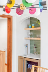 Rainbow Mid Century modern inspired chandelier in dining room with a bar nook that has light wood open shelving and stacked green avocado tiles.