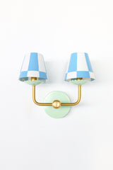 A double wall sconce that turns a classic silhouette playful. The Double Adele Sconce pairs a mint green backplate and brass arms with two tapered shades in a bold sky blue and white checkerboard print, a preppy, graphic look that reads collected rather than matchy. A strong pick for a bedroom, hallway, or powder room that wants pattern with its color.