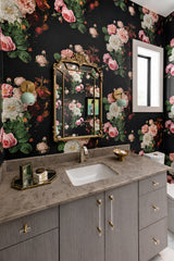 Maximalist powder room with dramatic dark floral wallpaper, a gray vanity with brass hardware, and a pair of mint green Loa globe wall sconces in warm brass. An ornate vintage-style gold mirror and marble-look countertop create bold, eclectic bathroom decor, perfect for statement bathroom vanity lighting and colorful wall sconce styling.