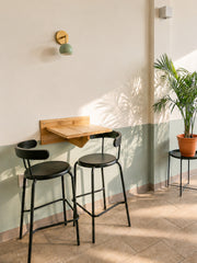 Cafe corner seating with mint & brass Loa sconce and palm plant
Description: Small cafe seating vignette featuring a mint green Loa wall sconce with brass hardware above a wall-mounted wood table and black chairs. Clean white walls, soft sage lower wall, tiled floor, and a potted palm add breezy modern style. Great for Pinterest searches like cafe lighting ideas, mint wall sconce, brass sconce, and modern bistro interior.