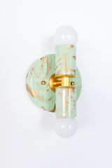 A close product photo of the Small Thalia Sconce in a mint, cream, and gold hand-marbled finish, shown in three unique variations to highlight the handmade patterning. The small two-bulb wall light has a soft, decorative look that works well in powder rooms, kids bathrooms, colorful hallways, and vanity spaces. Its pale green marbling, warm gold hardware, and compact shape make it a sweet fit for chinoiserie decor, grandmillennial style, and muted maximalist interiors.