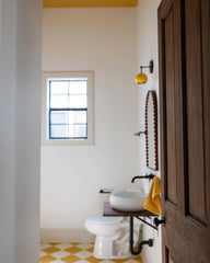 Bathroom remodel with black and mustard wall sconce designed and made by sazerac stitches in new Orleans. Features a midcentury modern style globe, mustard and cream patterned floors, white walls, cream accents.