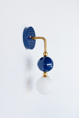 A statement wall sconce for rooms that lead with deep, classic color. This angle of the Ida sconce puts the bold round navy backplate front and center, with a brass arm curving down to a glossy navy sphere and frosted glass globe. Grounded, confident, and timeless, it's a classic pick for coastal bathrooms, powder rooms, bedrooms, and traditional spaces that want one crisp, standout detail.