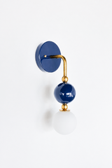 A deep navy wall sconce for a coastal bath, powder room, or bedroom that leads with timeless color. This view of the Ida sconce highlights the bold navy backplate and the brass arm curving down to a glossy navy sphere and frosted glass globe. Crisp, grounded, and confident, it's a classic pick for coastal traditional, grandmillennial, Southern masculine, and colorful traditional homes.