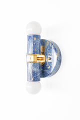 Close-up view of the Thalia sconce featuring a marbled blue-and-cream surface with gold accents and polished brass hardware. The clean geometric silhouette makes it easy to use in bathrooms, hallways, bedrooms, and powder rooms.