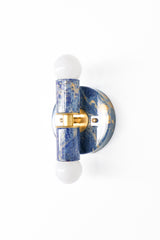 A colorful marbled wall light with a round backplate and cylindrical center, finished in rich navy and bright blue tones with creamy highlights. Handmade marbling ensures natural variation from piece to piece, like wearable art for your walls