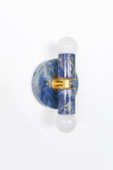 Detail shot of a handcrafted marbled Thalia wall sconce in layered blues with cream and gold splashes. The glossy finish and simple form create a high-impact statement light that pairs well with tile, wallpaper, or crisp white walls.