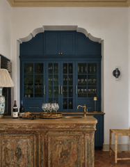 Navy, cream, and gold marbled Thalia wall sconce with raw brass hardware shown unlit on a white wall in a high-end home bar. Deep navy glass-front cabinetry with brass hardware, rustic reclaimed wood island, brass bar faucet, terracotta floor, and styled wine and glassware. Blue marbled wall light for kitchen, wet bar, butler’s pantry, or dining nook. Eclectic, grand millennial, coastal color story with artisan handmade statement lighting.