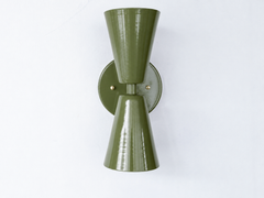 A statement wall sconce for rooms that lead with warm, earthy color and sculptural shapes. This angle of the Dryades sconce shows off its olive-green double-cone silhouette — one cone throwing light up, one down — meeting at a narrow waist on a round olive backplate with a brass screw accent. Grounded, rich, and a little 70s, it's a confident pick for hallways, libraries, dens, and mid-century or organic modern interiors that want earthy color with crisp lines.