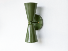 A deep olive-green double-cone wall sconce for a hallway, library, bar, or mid-century modern room that wants earthy color and crisp lines. Shown straight on, the Dryades sconce pairs an upward and a downward olive cone at a narrow waist on a round olive backplate, with warm brass screw accents. Grounded, rich, and a little retro, its bowtie silhouette suits 70s-inspired, organic modern, masculine, and moody traditional spaces.