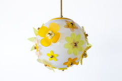 Side view of one-of-a-kind floral acrylic pendant, white globe with layered blossoms in lemon, marbled buttercream, and goldenrod, each petal pinned with warm metal hardware; playful midcentury vibe, handmade in New Orleans
