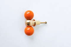 A double-ball drawer pull pairing two glossy orange spheres with a polished brass ball at the center, shown at an angle to show its full shape. A confident, citrusy pick for a bold kitchen, a playful bathroom, or any cabinetry that wants real color instead of playing it safe.