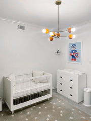 Neutral nursery design with an orange and brass midcentury modern style chandelier