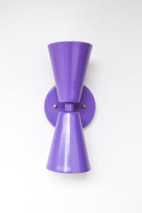 Front-facing image of the Dryades Sconce in a bright orchid purple, featuring clean lines, matte powder coat finish, and flared cone shades that evoke midcentury and Art Deco lighting. The symmetrical design and rich color bring energy and personality to interior spaces, ideal for color-drenched rooms or bold lighting schemes.