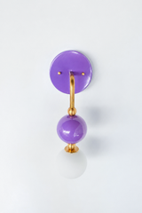 A bright orchid-purple wall sconce for a girl's bedroom, playful powder room, or maximalist bathroom with real personality. Shown straight on, the Ida sconce stacks a glossy purple powder-coated sphere over a frosted glass globe, joined by warm brass hardware and a round purple backplate. The head-on view shows how the spheres line up into a tidy vertical drop. Saturated and joyful, it's a fearless pick for grandmillennial, eclectic, and colorful traditional spaces.