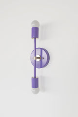 Angled product photo of the Orchid Medium Thalia Sconce with polished chrome accents and white globe bulbs. The vertical two-light design feels clean, colorful, and slightly retro, with a narrow silhouette that works well beside bathroom mirrors, in small powder rooms, kids spaces, guest bathrooms, hallways, or playful modern and grandmillennial interiors.