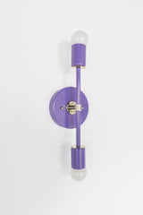 The Orchid Medium Thalia Sconce pairs a glossy purple finish with polished chrome hardware and two exposed globe bulbs. Its slim vertical shape works beautifully as a bathroom vanity sconce, hallway light, bedside wall light, or colorful accent fixture for playful modern interiors.