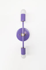 Purple double-globe wall sconce with polished chrome hardware, shown as the Orchid and chrome Medium Thalia Sconce. The tall vertical shape, round backplate, exposed bulbs, and glossy powder-coated finish make it a fun choice for colorful bathroom lighting, kids bathroom sconces, powder room vanity lights, hallway lighting, bedroom sconces, and modern eclectic interiors.