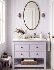 Paired on either side of an oval mirror, these lavender marbled Thalia sconces bring a soft, romantic accent to this pastel bathroom. The pale purple vanity, floral arrangement, and delicate wallpaper all play into the feminine palette, while the sconces add just enough contrast and shine with their warm brass center details.