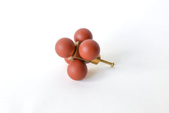 A sculptural oversized drawer pull made with five smooth, matte terra cotta-colored resin spheres arranged around a solid brass cube core. This bold and modern cabinet knob is designed to make a statement, adding an artistic and architectural touch to any dresser, credenza, or built-in cabinetry. Shown on a clean white background to highlight its form and contrast in texture and material.