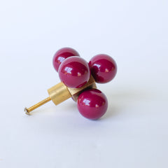 Add a vibrant and whimsical touch to your furniture with the Oversized Ball Cube Knob by Sazerac Stitches. This unique drawer pull features four striking Black Cherry balls set in a brass cube, blending modern flair with a bold pop of color. Ideal for giving cabinets and drawers a fun, stylish upgrade.