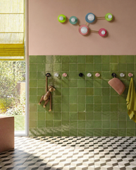 A playful yet elevated kids bathroom with glossy handmade-look green wall tile, blush pink upper walls, a graphic patterned floor, and cheerful accents that feel colorful, polished, and gender neutral. The Taurus sconce by Sazerac Stitches is installed above the hooks in a fun multicolor palette, bringing in a constellation-inspired shape and a sophisticated rainbow effect that feels artful rather than overly childish. This image works beautifully for searches like colorful kids bathroom ideas, luxury kids 
