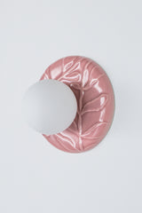 Angled product photo of pastel pink ceramic floral leaf relief sconce with frosted globe, decorative chinoiserie style wall light with feminine charm, ideal as a bedside sconce, vanity lighting, or hallway accent.