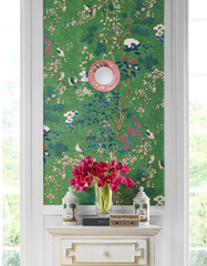 Styled interior vignette featuring the Pastel Pink Lierre ceramic wall sconce by Sazerac Stitches, with a glossy blush-pink botanical leaf relief backplate and a white globe diffuser. The sconce is centered on emerald green chinoiserie wallpaper with flowering branches and birds, framed by tall white-trim windows. Below, a vintage white console holds ginger jar–style decor and a clear vase of hot pink tulips, creating a colorful grandmillennial, maximalist, designer look perfect for an entryway, hallway, or