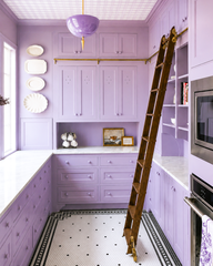 Proof that purple can be sophisticated, this butler's pantry wraps lavender cabinetry from floor to ceiling and tops it with a soft gingham-papered ceiling for a sweet, unexpected finish. A walnut rolling library ladder on a brass rail adds warmth and old-house function, while marble counters, a graphic black and white mosaic floor, and a collection of white ironstone platters keep the room feeling collected and layered. The orchid Alexander Pendant crowns it all, its glossy domed shade and brass finial pul