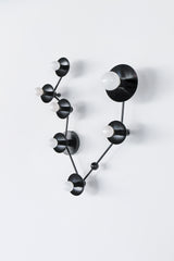 Angled view of a Pisces star sign wall light in matte black featuring powder-coated steel saucer discs and opal-style white globe bulbs on a branching constellation layout; statement modern wall sconce for bold interior design, contemporary bathroom lighting, dark academia decor, minimalist but edgy hallway lighting, or high-contrast black-and-white powder room.