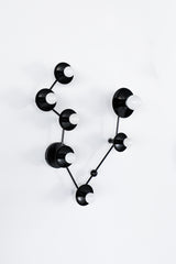 Matte black Pisces constellation wall sconce with powder-coated steel discs and small white globe bulbs on branching metal arms; modern zodiac star sign light fixture with sculptural, celestial design for a moody bathroom vanity, dramatic powder room, eclectic entryway, or maximalist gallery wall lighting.