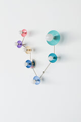 Angled view of the Pisces constellation wall light, a zodiac inspired modern sconce with chrome arms and powder coated steel disc shades in pastel and bright colors including blush pink, orchid, cream, denim blue, celestial teal, and poolside aqua, paired with white globe bulbs. Statement wall sconce for eclectic interiors, colorful bathroom vanity lighting, feminine powder room decor, maximalist design lighting, modern kids room wall light, playful contemporary home decor, mid century modern style sculptur