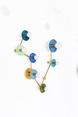 Angled close view of Pisces constellation wall sconce showing powder-coated steel disc shades in teal, mint, denim, hydrangea blue, and Mediterranean blue with brass arms and white globe bulbs; artistic celestial lighting that reads like wall art, great for maximalist bathrooms, modern coastal homes, eclectic interiors, colorful hallway lighting, and statement bedroom sconces, a zodiac-inspired mid century modern fixture with bold color pops.