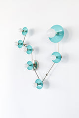 Angled view of Pisces constellation light fixture in Poolside blue and chrome, with sculptural branching arms, powder-coated steel disc backplates, and round globe bulbs; statement wall lighting with mid century modern vibe for an artful bathroom sconce over a mirror, fun powder room lighting, coastal color pop decor, and bold maximalist style.