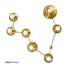 Front view of the Pisces constellation wall light in raw brass, arranged like a star map with seven small white globe bulbs and circular metal disc shades; bold celestial zodiac lighting for a modern bathroom, chic powder room, or contemporary living space, perfect for design lovers searching for constellation sconce, astrology decor, sculptural wall lighting, statement hallway light, and playful maximalist interior style.