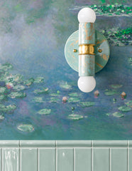 Poolside, Cream, and Gold hand-marbled Small Thalia Sconce shown vertically on dreamy blue-green waterlily wallpaper above glossy pale green bathroom tile. The soft aqua marbling, cream accents, brass hardware, and white globe bulbs give this petite two-light wall sconce a custom, small-batch feel that works beautifully in colorful bathrooms, powder rooms, kids baths, cottage bathrooms, grandmillennial interiors, watery coastal spaces, and wallpapered rooms with muted blue and green palettes.