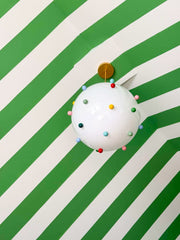 Rainbow gumball chandelier pendant with a white glass globe, multicolor dot accents, and warm brass hardware, styled in a vibrant green kids playroom with dramatic green and white striped ceiling, large windows with cream curtains, and playful seating, ideal for eclectic and preppy interiors, maximalist family homes, and statement kids room ceiling lighting.