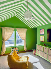 Rainbow gumball globe pendant light with a white glass sphere, colorful round accent knobs, and a brass canopy and downrod, hanging in a bold green kids playroom with a green and white striped ceiling, built-in storage, and playful maximalist decor, perfect for design-forward families who love colorful modern lighting.