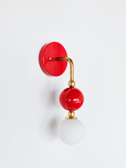 Bold vanity lighting that gives a bathroom or powder room real personality. Seen in profile, the Ida sconce shows off its curved brass arm reaching from a glossy cherry-red backplate down to a stacked red sphere and frosted glass globe. The side view highlights the brass ball detailing and how far the fixture projects off the wall. A confident, saturated choice for eclectic, maximalist, and bold graphic interiors.