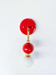 A statement wall sconce for rooms that lead with saturated color. This angle of the Ida sconce puts the bold round red backplate front and center, with a brass arm curving down to a glossy cherry-red sphere and frosted glass globe. High-gloss, high-contrast, and confident, it's a playful pick for colorful bathrooms, powder rooms, entryways, and maximalist spaces that want one arresting, joyful detail.