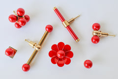 A lineup of red cabinet hardware in five different shapes, from a multi-ball cluster knob and a long bar pull to a small double gumball knob, a single ball knob, and a scalloped flower knob, all finished with brass posts and backplates. A good one-stop reference for mixing pull styles across different drawer and cabinet sizes without losing the color story.