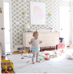 Light-filled kids room featuring two mint green Loa wall sconces in brass mounted on a black-and-white patterned wallpaper accent wall. A white dresser, playful toys, and a large pastel art print create a cheerful, lived-in space. Perfect for searches like kids room lighting, nursery wall sconce, mint green brass sconce, and modern playful interior decor.