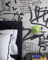 This boy's bedroom wraps the wall in a hand-lettered, black and white graffiti mural, the kind of backdrop that reads more like a rock poster than typical kids' decor. The Sid Sconce mounted bedside brings a sharp jolt of chartreuse and gold, its spiked dome giving the whole room a bit of an edge. A black velvet headboard and a nightstand styled with books and a Rubik's cube keep it grounded in an actual kid's life, not just a design statement.
