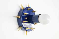 Angled product photo of the Sid Sconce in glossy navy with gold-tone spikes and a white globe bulb. This view shows the fixture’s compact round shape, hand-drilled spike details, and unexpected mix of polished color and glam-punk hardware.