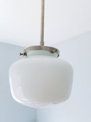 This is the fixture for the kitchen you actually want to cook in—where efficiency meets aesthetic grace. The schoolhouse glass shade, suspended clean from a brushed nickel canopy, creates an almost Scandinavian clarity: form following function, nothing wasted, everything essential. The gently rounded dome catches and diffuses light with architectural intention, casting a gentle wash across counters and workspace. There's an honesty to this pendant that contemporary kitchens crave—the compressed dome silhoue
