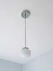 This is the fixture for the kitchen you actually want to cook in—where efficiency meets aesthetic grace. The schoolhouse glass shade, suspended clean from a brushed nickel canopy, creates an almost Scandinavian clarity: form following function, nothing wasted, everything essential. The gently rounded dome catches and diffuses light with architectural intention, casting a gentle wash across counters and workspace. There's an honesty to this pendant that contemporary kitchens crave—the compressed dome silhoue