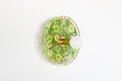 Modern two light wall sconce with brass hardware and green flowers. Features resin-encapsulated orange flowers with greenery, ferns, and leaves.  Adds a real-like nature theme to any interior design project.  Called the Botanico Sconce by Sazerac Stitches. Features green flowers with greenery