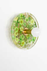 Modern two light wall sconce with brass hardware and flowers. Features resin-encapsulated orange flowers with greenery, ferns, and leaves.  Adds a real-like nature theme to any interior design project.  Called the Botanico Sconce by Sazerac Stitches. Features green flowers with greenery